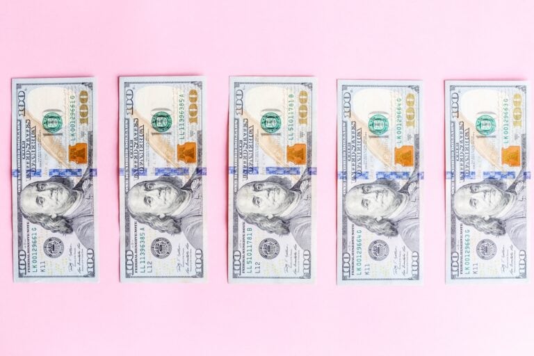 $100 bills laid out on pink background for financial or business concept.